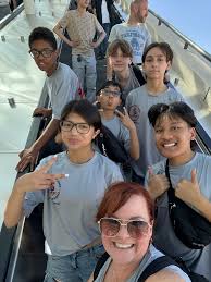 Doral Academy students on a trip together, smiling on an escalator.