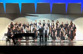 Students performing on stage with the Pebble choir, directed at a piano.